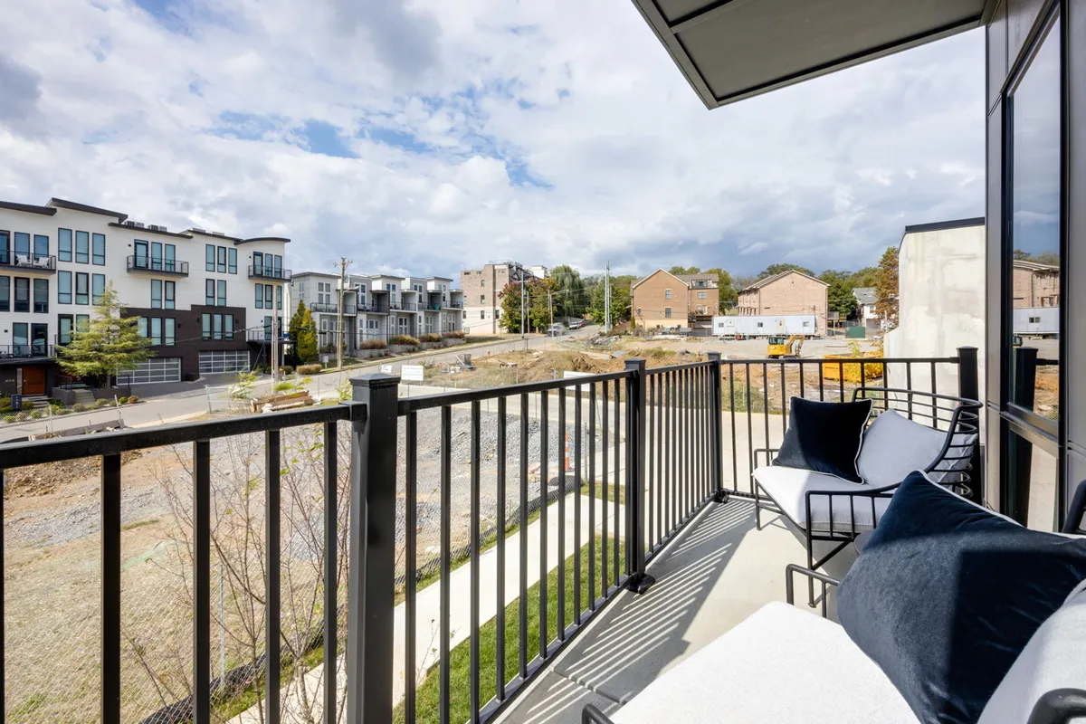 A private balcony with comfortable seating overlooks neighboring buildings and landscaped areas, evoking a sense of contemporary relaxation. The balcony is ideal for unwinding with a morning coffee, enjoying city views, or social moments under the stars.