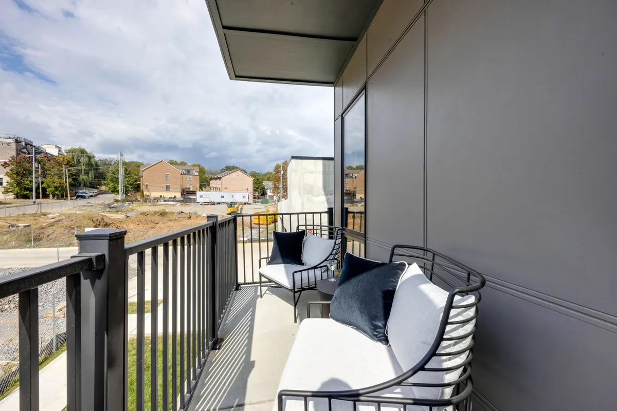 A calm balcony seating area overlooking the neighborhood, with modern railings and a peaceful ambiance. The view connects indoor comfort to the outdoor urban landscape, emphasizing the retreat aspect after a day of city exploration.