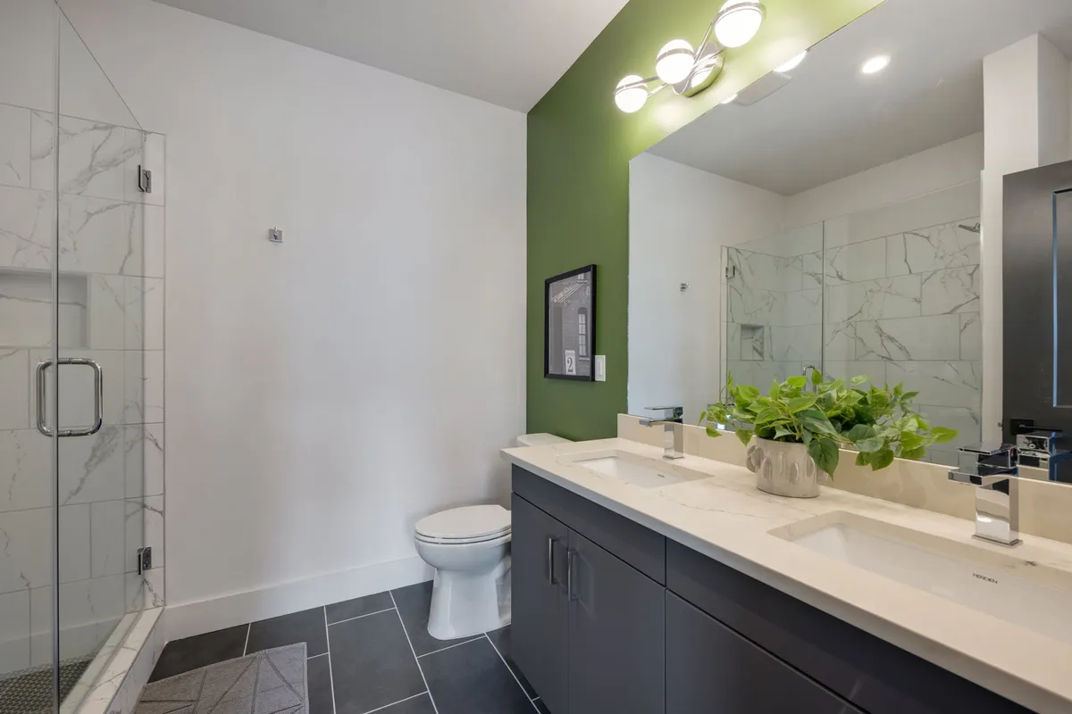 A modern bathroom featuring a sleek vanity, glass shower enclosure, green accent wall, and a mirrored medicine cabinet. The design is fresh and rejuvenating, evoking a spa-like atmosphere ideal for relaxation and personal care routines.