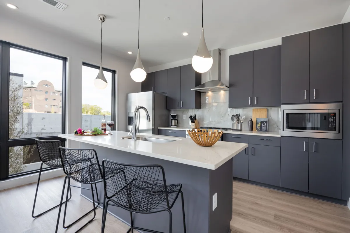 A spacious kitchen featuring a prominent kitchen island with chic black wire bar stools, stainless steel appliances, and warm pendant lighting. The setting highlights a breakfast bar ideal for morning coffee or casual meals, while the open layout encourages conversation.
